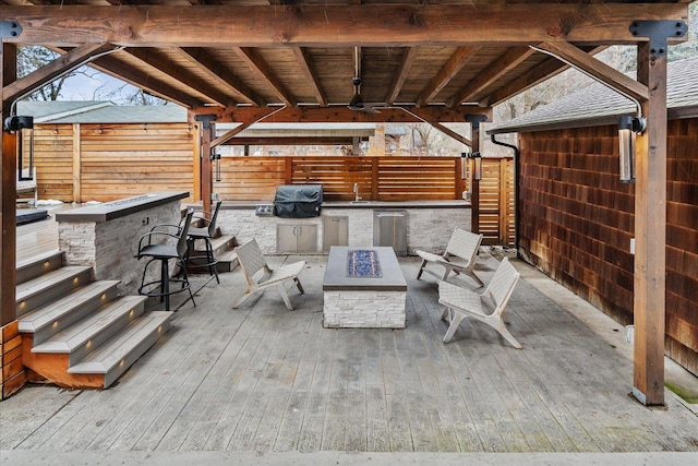 view of patio featuring a deck, a fire pit, a sink, fence, and exterior kitchen