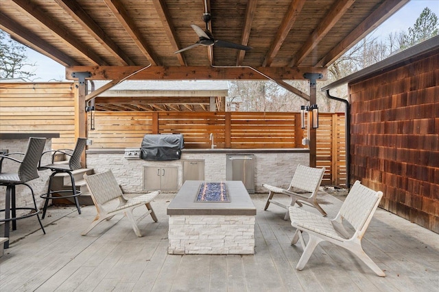 view of patio with an outdoor fire pit, area for grilling, ceiling fan, fence, and exterior kitchen