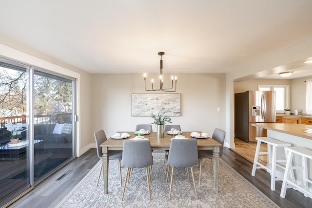 dining room with a notable chandelier, dark wood-type flooring, baseboards, and a healthy amount of sunlight