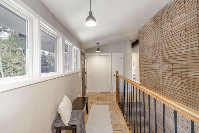 hall featuring lofted ceiling, brick wall, an upstairs landing, and stone tile floors