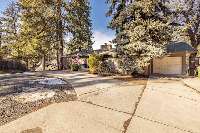 obstructed view of property with driveway, a chimney, an attached garage, and fence