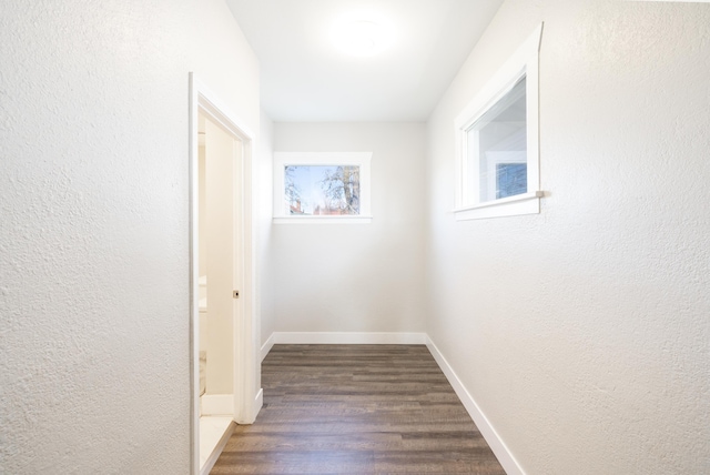 hall featuring a textured wall, dark wood finished floors, and baseboards