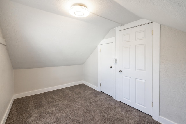 additional living space featuring lofted ceiling, dark carpet, a textured ceiling, and baseboards