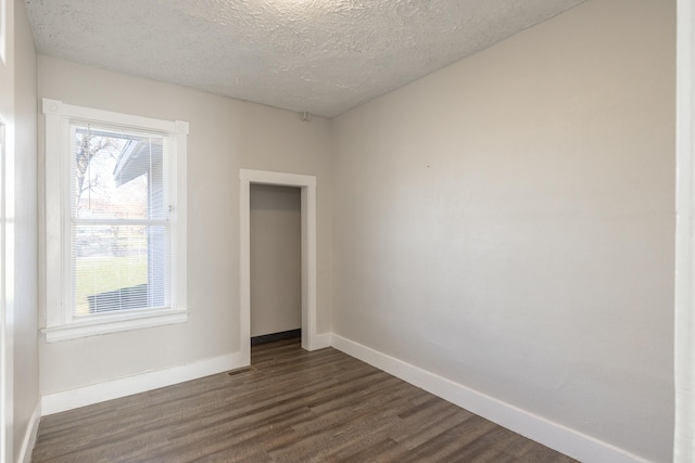 unfurnished room with a textured ceiling, dark wood-style flooring, visible vents, and baseboards