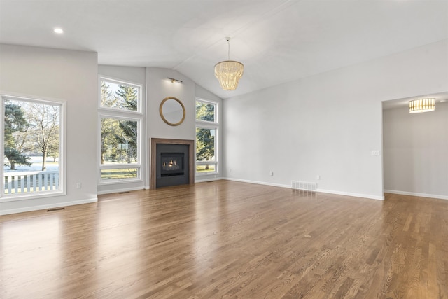 unfurnished living room with a glass covered fireplace, visible vents, a notable chandelier, and wood finished floors