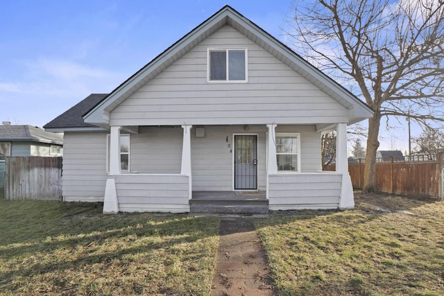 bungalow-style house featuring roof with shingles, a porch, a front lawn, and fence