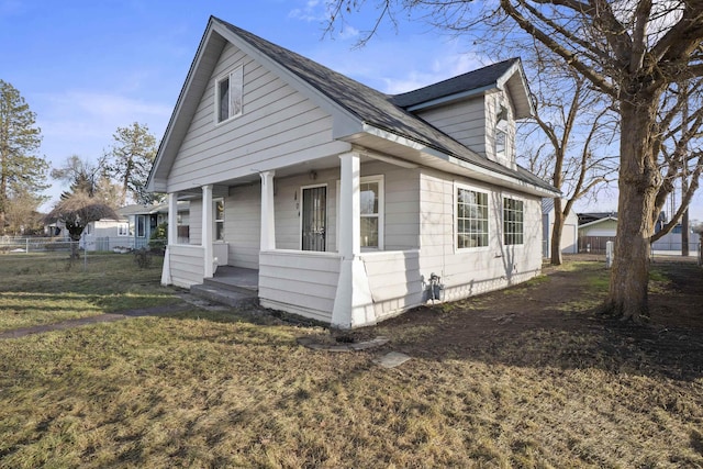 view of side of home with a porch, fence, and a lawn