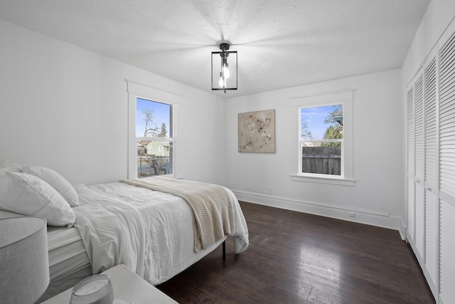 bedroom with a textured ceiling, multiple windows, wood-type flooring, and baseboards