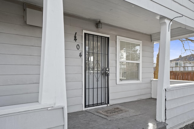 doorway to property with a porch and fence