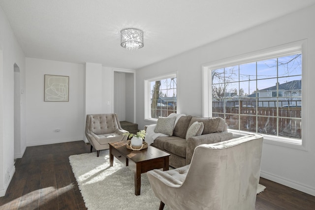 living room featuring baseboards, arched walkways, and dark wood-style flooring