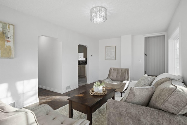 living area with arched walkways, visible vents, baseboards, and wood finished floors