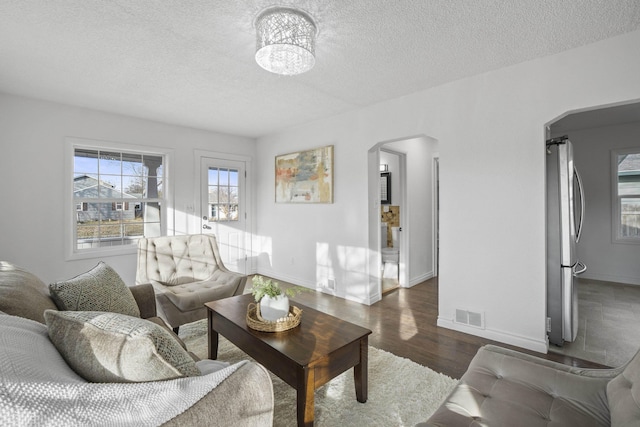 living room featuring baseboards, visible vents, arched walkways, wood finished floors, and a textured ceiling