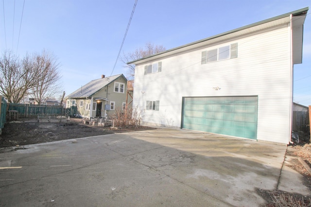 rear view of property featuring concrete driveway, fence, and an attached garage