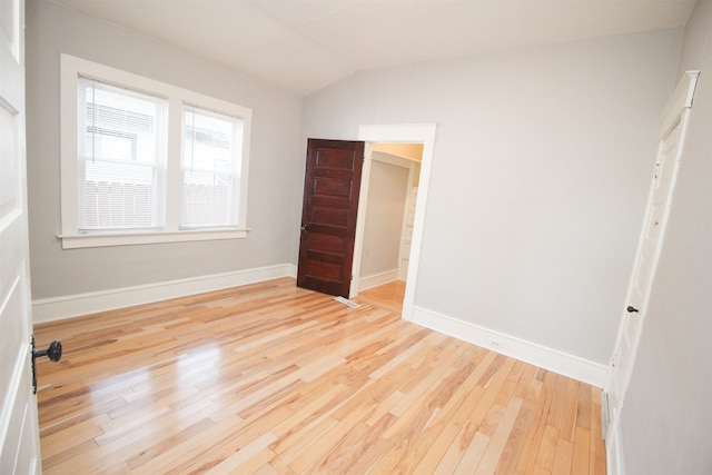 unfurnished bedroom with lofted ceiling, light wood finished floors, and baseboards