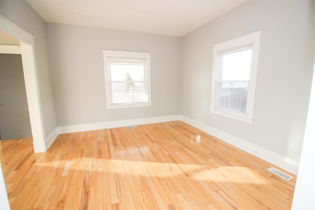 empty room featuring plenty of natural light, visible vents, light wood finished floors, and baseboards