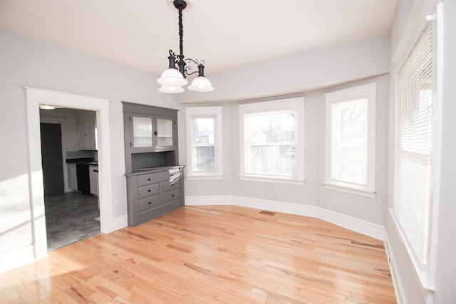 unfurnished dining area with a chandelier, a wealth of natural light, light wood-style flooring, baseboards, and visible vents