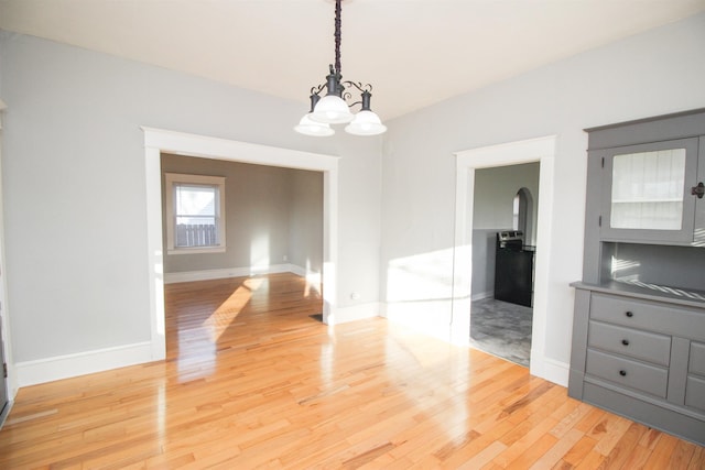 unfurnished dining area featuring baseboards, arched walkways, a chandelier, and light wood-style flooring