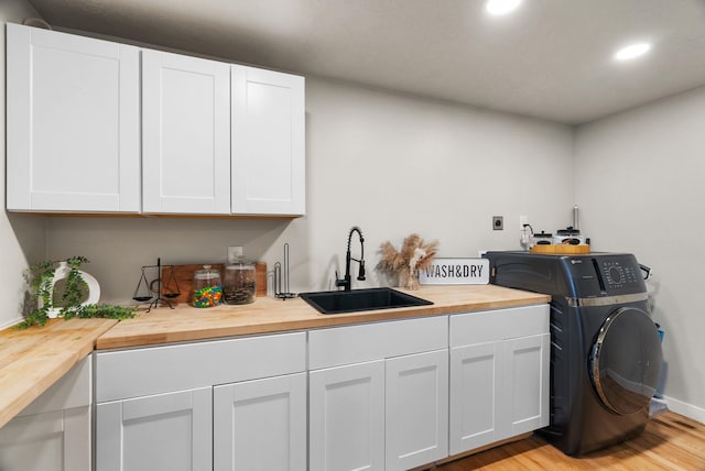 laundry area featuring cabinet space, washer / dryer, light wood-type flooring, a sink, and recessed lighting