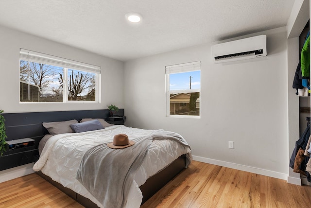 bedroom featuring an AC wall unit, light wood finished floors, multiple windows, and baseboards