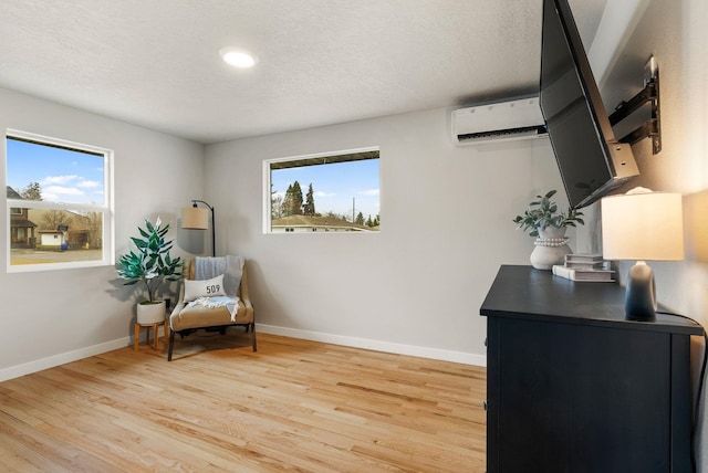 sitting room featuring light wood-style floors, a wealth of natural light, a wall unit AC, and baseboards