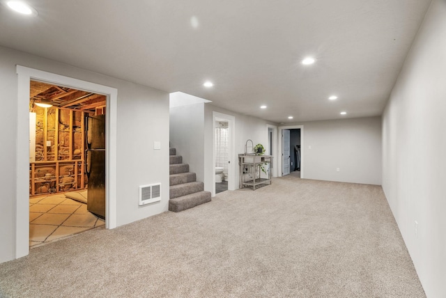 finished basement featuring carpet floors, stairway, visible vents, and freestanding refrigerator