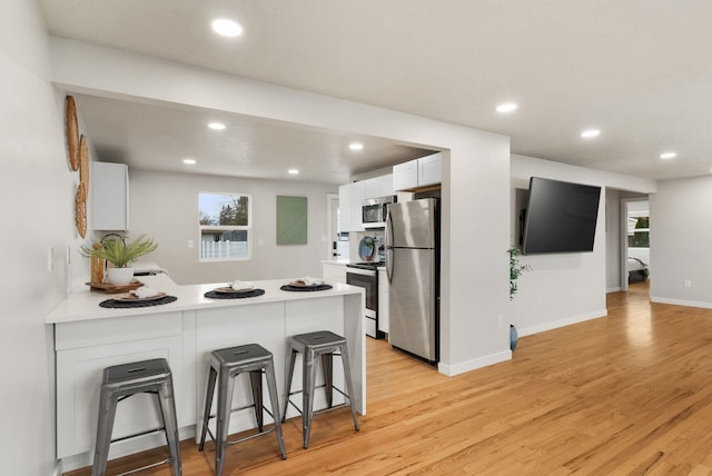 kitchen featuring a breakfast bar, white cabinetry, appliances with stainless steel finishes, and light countertops