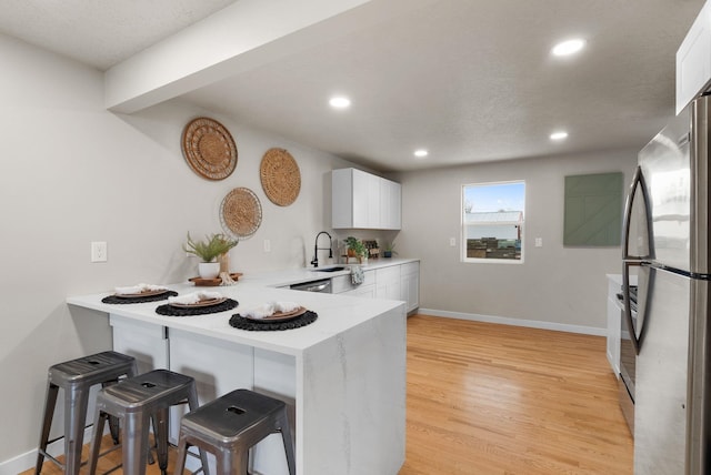 kitchen featuring light wood finished floors, white cabinets, a breakfast bar, freestanding refrigerator, and a peninsula