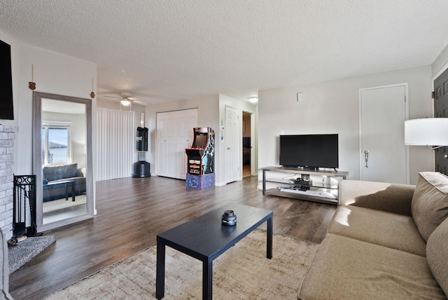 living area with a ceiling fan, a fireplace, a textured ceiling, and wood finished floors