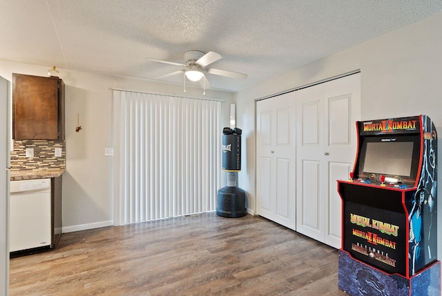 interior space with light wood-type flooring, a ceiling fan, baseboards, and a textured ceiling