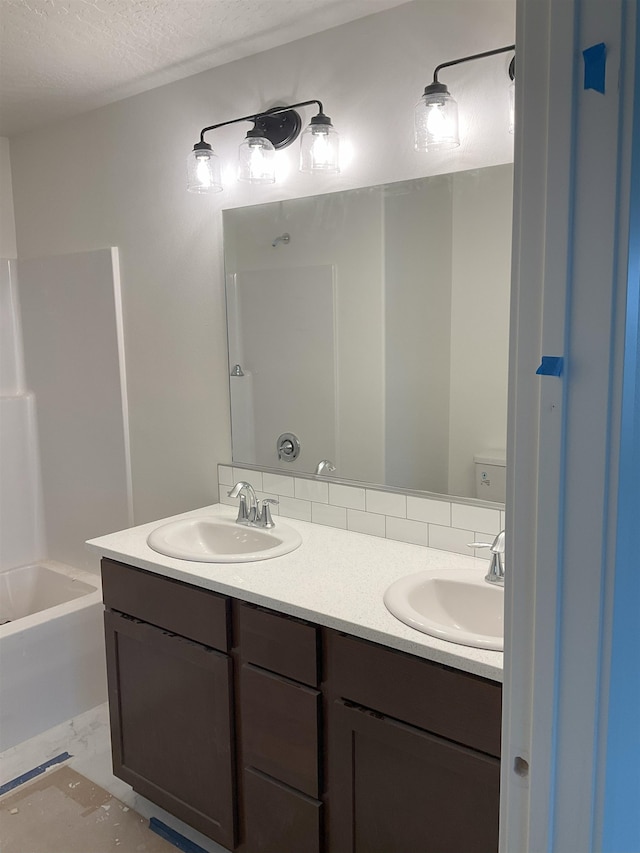 bathroom featuring a sink, a textured ceiling, toilet, and double vanity