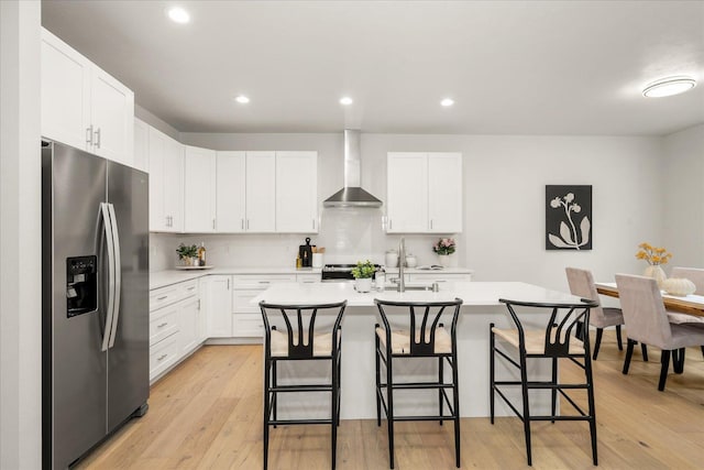 kitchen featuring a breakfast bar area, light wood finished floors, light countertops, appliances with stainless steel finishes, and wall chimney range hood