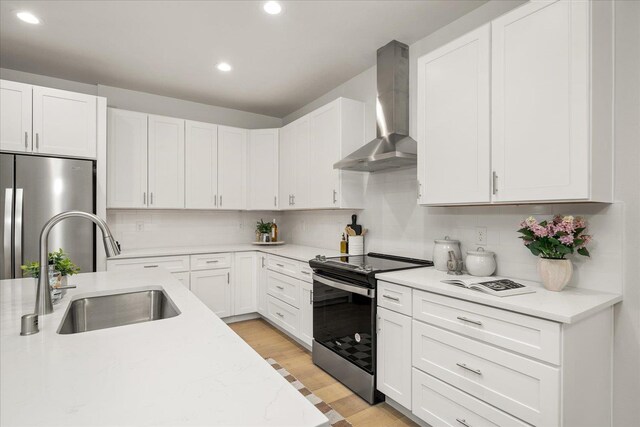 kitchen with light wood finished floors, stainless steel appliances, tasteful backsplash, a sink, and wall chimney exhaust hood