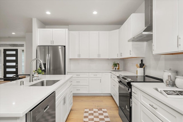 kitchen featuring a sink, light countertops, appliances with stainless steel finishes, and wall chimney range hood