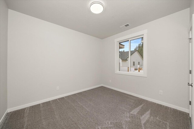 spare room featuring dark colored carpet, visible vents, and baseboards