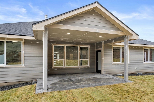 rear view of house with a shingled roof, a patio, and a lawn