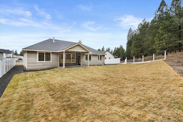 rear view of property featuring a shingled roof, a lawn, and fence