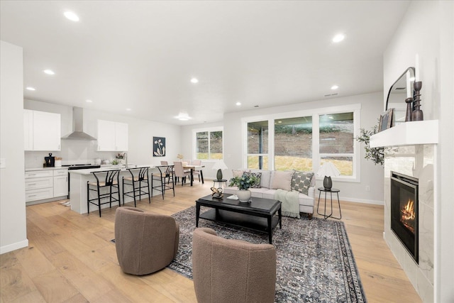 living room with light wood-type flooring, baseboards, a wealth of natural light, and a tile fireplace