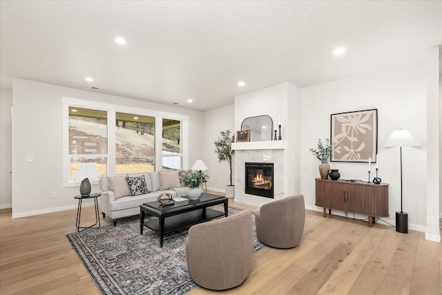 living area with recessed lighting, a premium fireplace, visible vents, baseboards, and light wood-type flooring