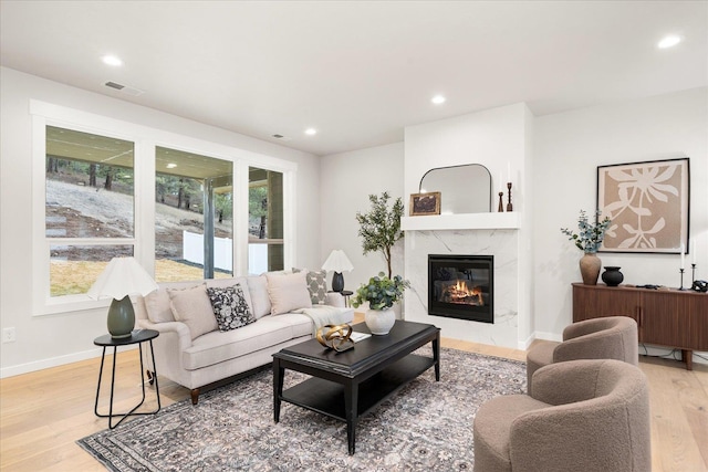 living room featuring light wood finished floors, visible vents, baseboards, a high end fireplace, and recessed lighting