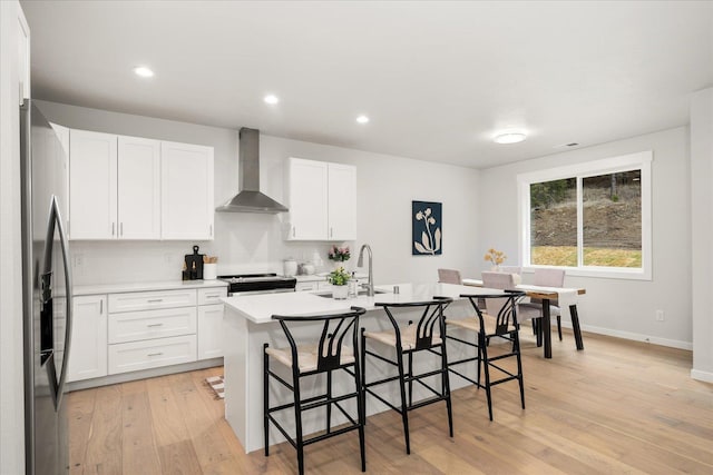 kitchen with a sink, wall chimney range hood, appliances with stainless steel finishes, an island with sink, and a kitchen bar