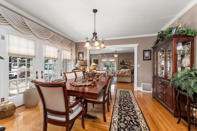 dining room with baseboards, visible vents, ornamental molding, light wood-type flooring, and a chandelier