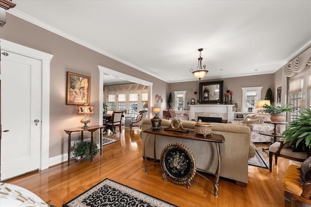 living room with baseboards, ornamental molding, a fireplace, and light wood-style floors