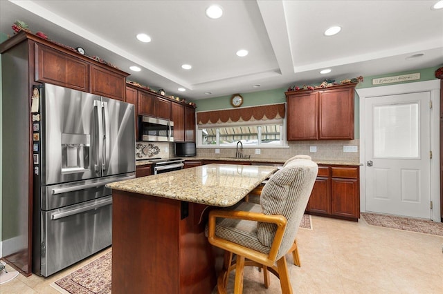 kitchen featuring stainless steel appliances, tasteful backsplash, a sink, a kitchen island, and light stone countertops