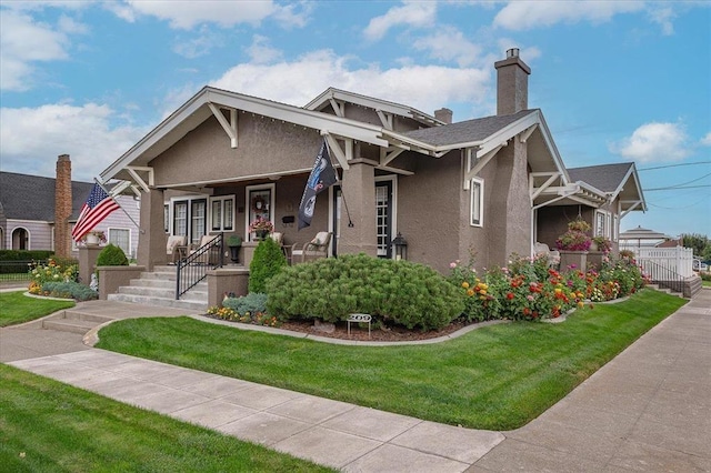 view of front facade with a front yard, a chimney, a porch, and stucco siding