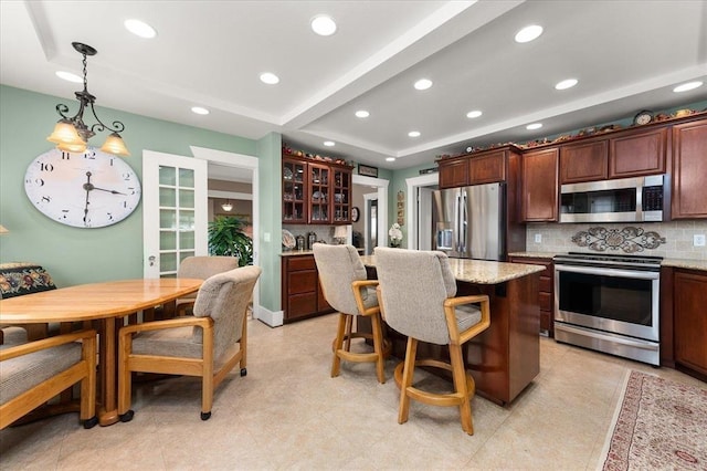 kitchen with tasteful backsplash, a raised ceiling, appliances with stainless steel finishes, glass insert cabinets, and a kitchen island