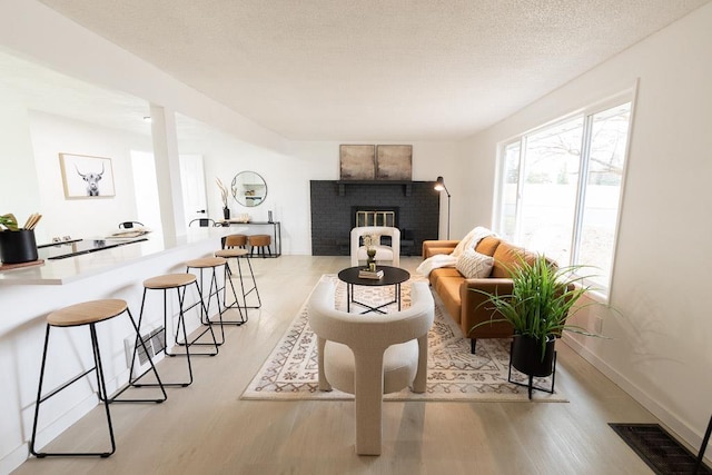 living area featuring a textured ceiling, wood finished floors, visible vents, baseboards, and a brick fireplace