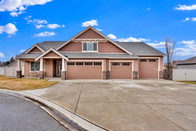 craftsman-style home with driveway, a garage, a shingled roof, stone siding, and fence