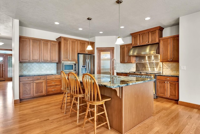 kitchen featuring under cabinet range hood, appliances with stainless steel finishes, brown cabinetry, and light wood finished floors