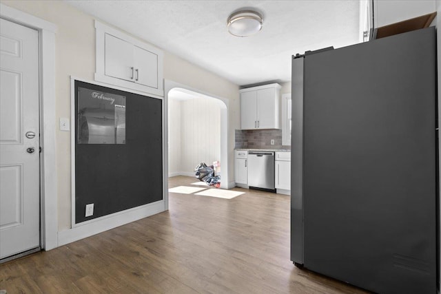 kitchen featuring arched walkways, stainless steel appliances, decorative backsplash, white cabinetry, and wood finished floors