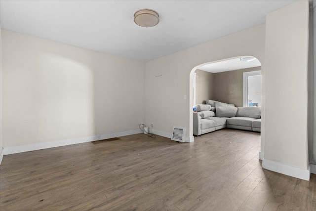 empty room with arched walkways, visible vents, baseboards, and wood finished floors